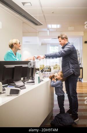 Side view of mature man giving id card to doctor while son standing by reception in hospital Stock Photo