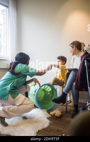 Pediatrician holding hands with boy while mother sitting in hospital Stock Photo