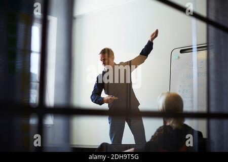 Businesswoman looking at male professional giving presentation against wall in board room seen from glass at creative of Stock Photo