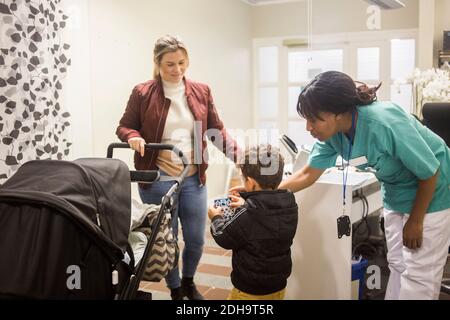 Pediatrician giving stickers to boy while mother standing with baby stroller in hospital Stock Photo