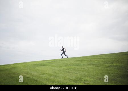 Side view of young man running on field against cloudy sky Stock Photo