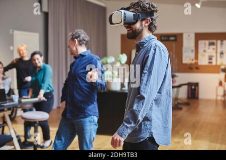 Businessman using virtual reality simulator while standing by colleagues in creative office Stock Photo