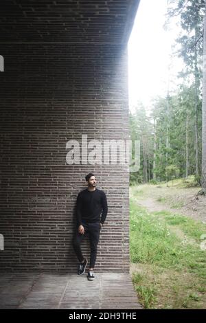 Full length of young man standing against brick wall Stock Photo