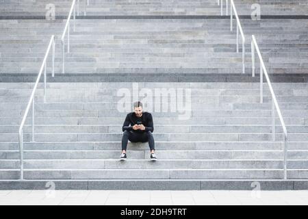 Young man using mobile phone while sitting on staircase Stock Photo