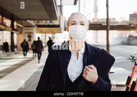 Businesswoman walking in street wearing face mask Stock Photo
