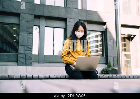 Businesswoman with face mask working using laptop Stock Photo