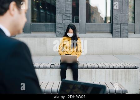 Businesspeople using laptop wearing face mask Stock Photo