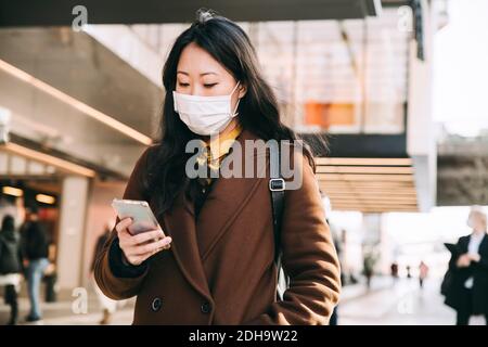 Woman walking in street with face mask using smartphone Stock Photo