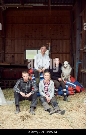 Siblings sitting with Australian Shepherd in barn Stock Photo