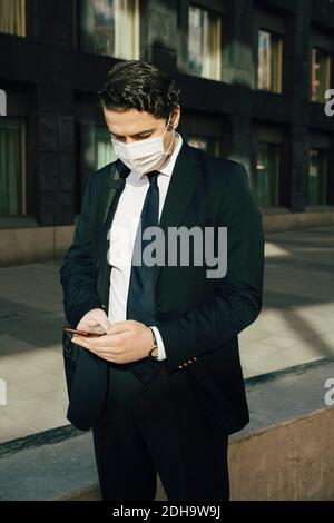 Businessman with face mask using smartphone Stock Photo