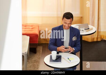 High angle view of smiling businessman using smart phone while standing in office Stock Photo