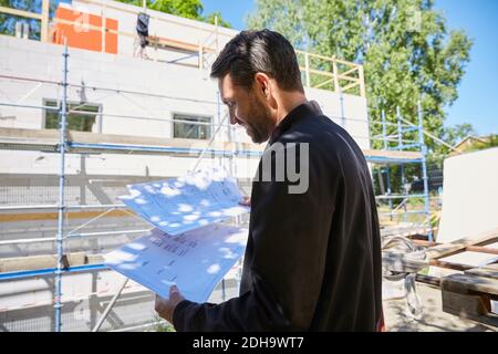 Businessman reading blueprints while standing at construction site on sunny day Stock Photo