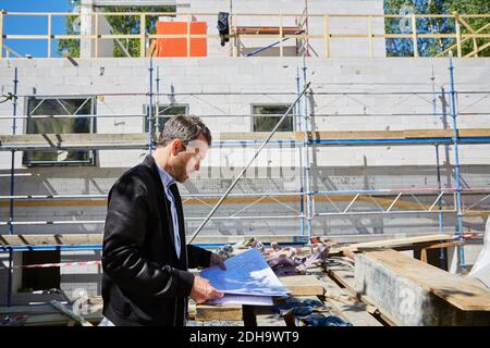 Side view of architect reading blueprint by incomplete building at construction site Stock Photo