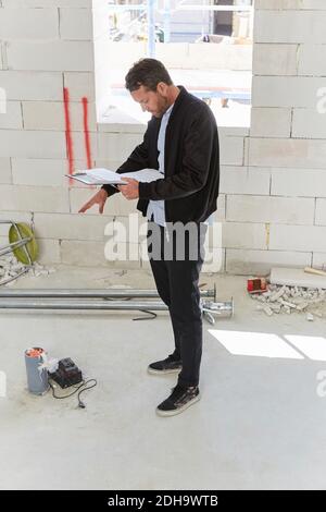Architect reading blueprint while planning at incomplete building Stock Photo