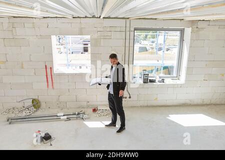Full length of architect with blueprint analyzing incomplete building Stock Photo