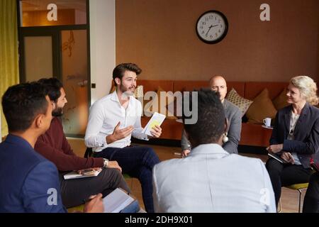 Male entrepreneurs discussing with coworkers while sitting in circle during office workshop Stock Photo