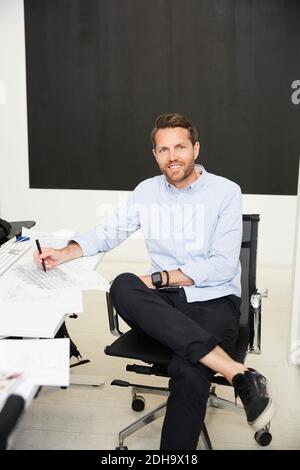 Portrait of confident architect with blueprints in creative office Stock Photo