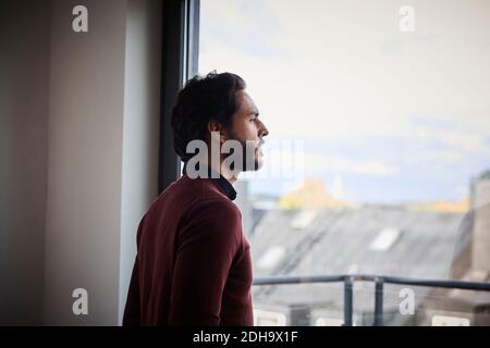 Contemplating businessman looking through window while standing in office Stock Photo