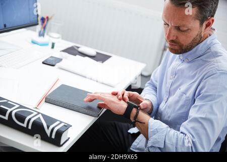 Businessman checking time while sitting at desk in creative office Stock Photo