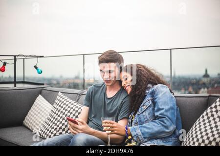 Smiling man showing smart phone to female partner with drink on terrace Stock Photo