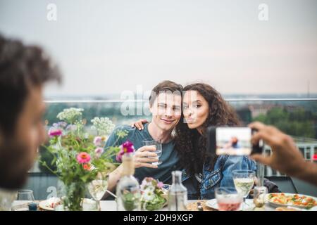 Cropped hand of man clicking photograph of couple through phone on terrace during party Stock Photo