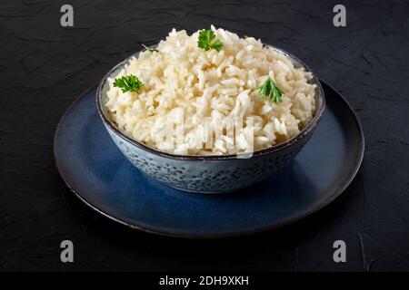 Cooked rice with fresh parsley leaves, in a bowl, on a dark background Stock Photo