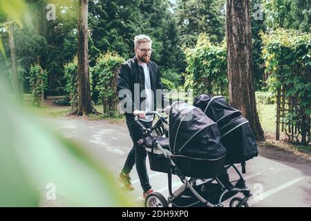 Full length of man pushing baby carriage on footpath Stock Photo