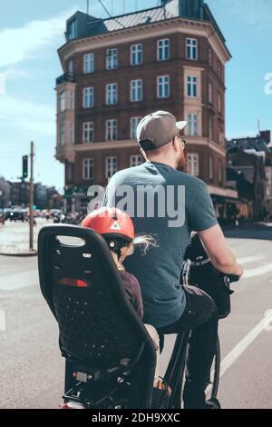 Rear view of father cycling while daughter sitting on back seat in city Stock Photo