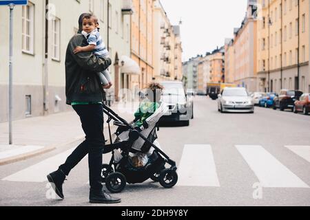 Father crossing road with children while pushing baby stroller in city Stock Photo