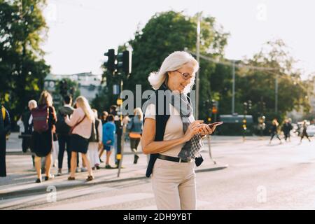 Smiling wrinkled female using smart phone on road in city Stock Photo