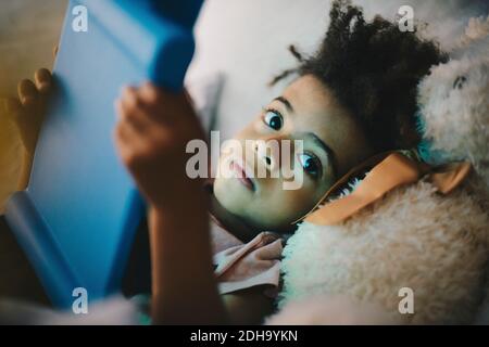 Portrait of boy using digital tablet while lying with teddy bear on bed at home Stock Photo