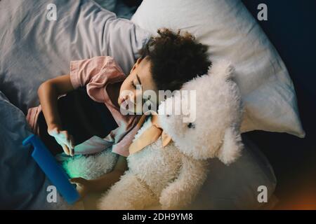 High angle view of boy lying with teddy bear while using digital tablet on bed at home Stock Photo