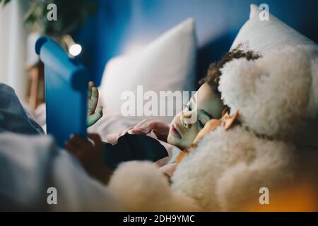 Boy lying with teddy bear while using digital tablet on bed at home Stock Photo