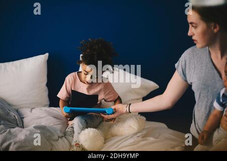 Mother carrying toddler giving digital tablet to son at home Stock Photo