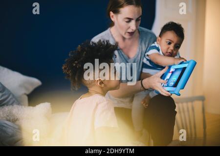 Mother carrying son while showing digital tablet to boy at home Stock Photo