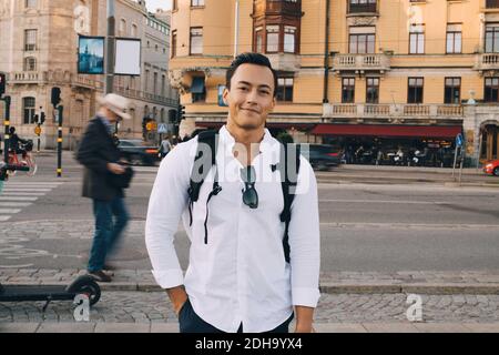 Portrait of smiling young man with hand in pocket standing against building Stock Photo