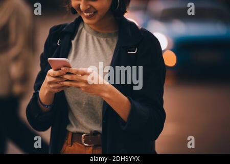 Midsection of smiling young woman using social media on phone while standing in city Stock Photo