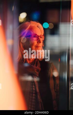 Senior woman looking away while standing in city at night Stock Photo