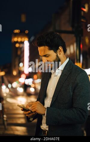 Man using smart phone while standing in city at night Stock Photo