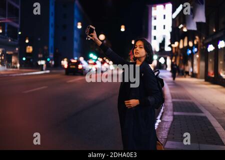 Young woman with phone hailing for taxi in city at night Stock Photo