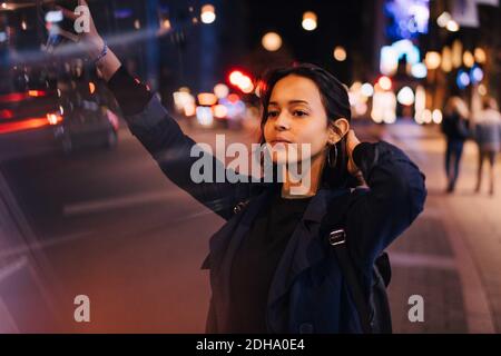 Young woman with hand in hair hailing for taxi in city at night Stock Photo