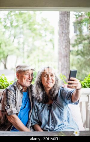 Smiling senior couple taking selfie in porch Stock Photo