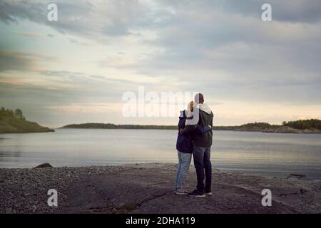 Rear view of couple standing at beach while looking at lake against sky during sunset Stock Photo