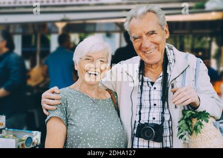 Portrait of smiling senior couple with arm around standing at market in city Stock Photo