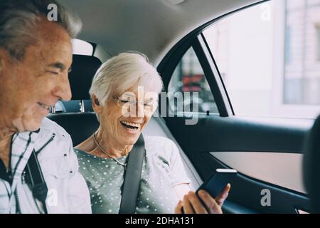 Smiling retired couple using mobile phone while sitting in car during vacation Stock Photo