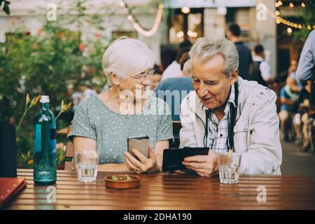 Retired couple using mobile phone while sitting at restaurant in city Stock Photo