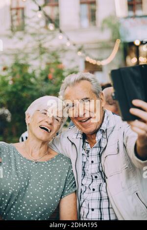 Senior man taking selfie with happy woman while sitting at restaurant in city Stock Photo