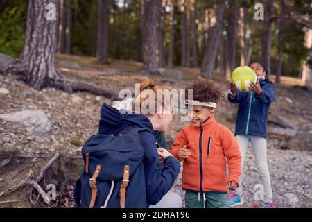 Mother looking at smiling boy wearing headlamp while daughter playing with soccer ball in background Stock Photo