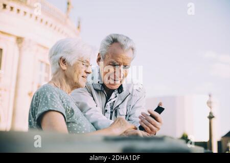 Senior male and female tourists using smart phone while standing in city against sky Stock Photo