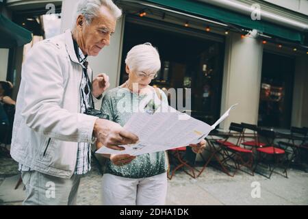 Senior couple reading map while standing on sidewalk in city during vacation Stock Photo